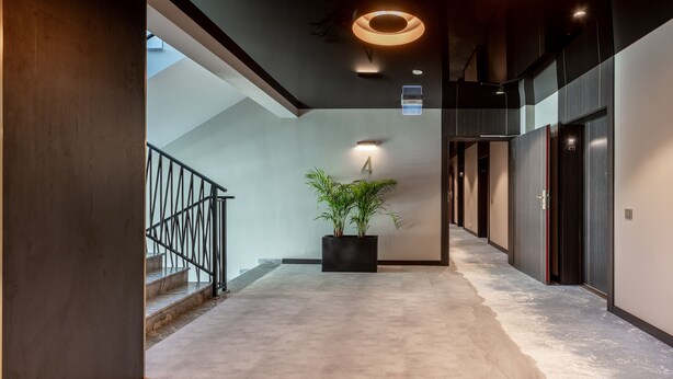 Een moderne hal met een trap, een potplant en een bordje met kamer nummer 4.