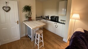 A compact kitchen with a white countertop, a sink, a stove, and a microwave. There's a potted plant and a heart-shaped decoration on the wall. - Converted Stables - Pet Friendly - Enclosed Garden (Pontefract)