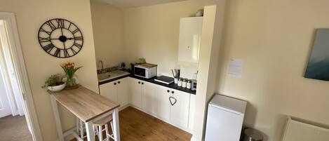 A compact kitchen with white cabinets, a wooden countertop, a sink, a microwave, and a refrigerator.