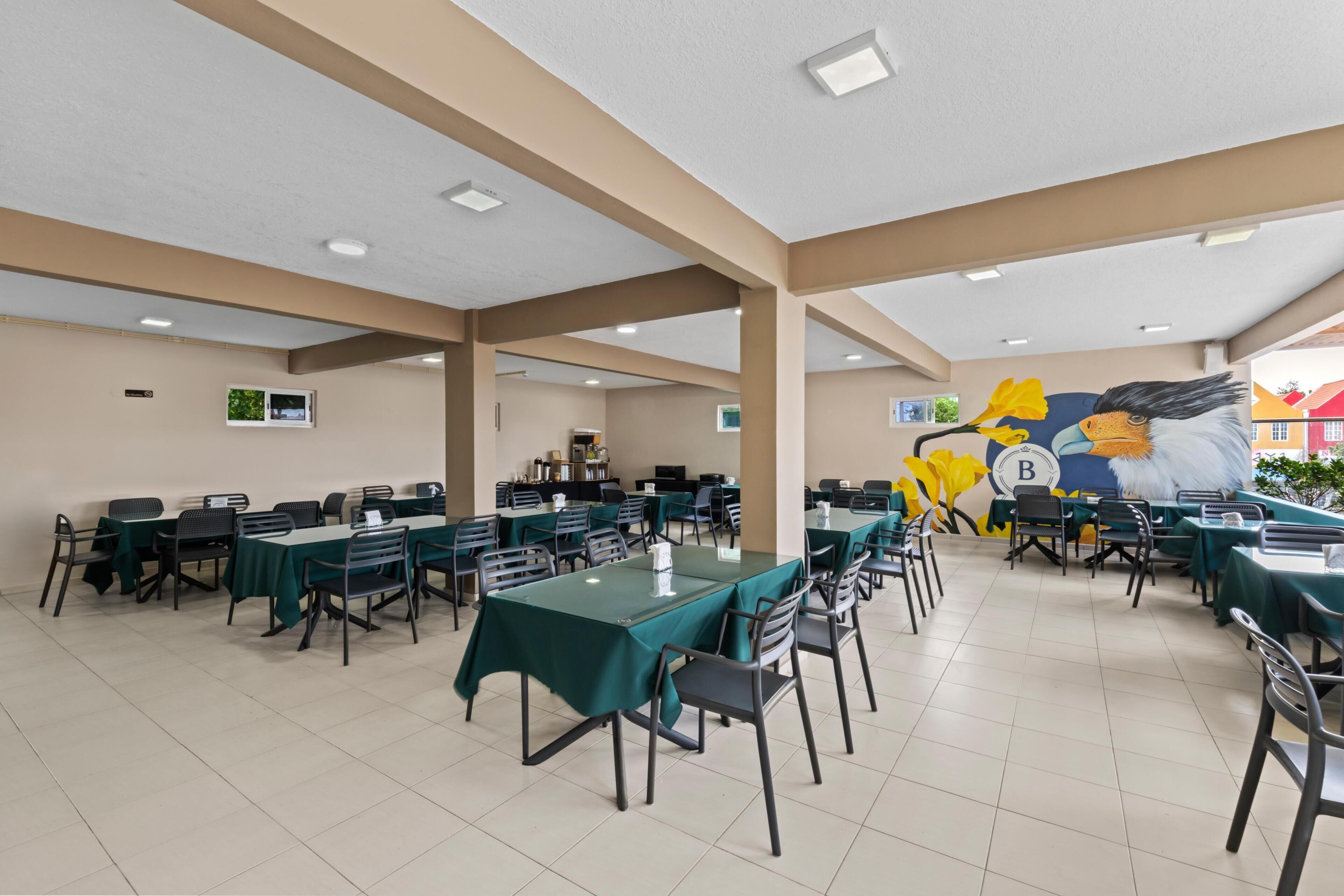 Un amplio comedor interior con varias mesas y sillas, techo alto con iluminación empotrada y un mural en la pared.