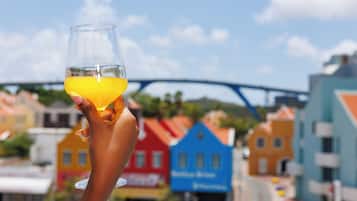 A hand holding a glass of orange juice with colorful buildings in the background.