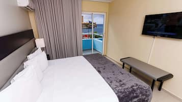A hotel room with a bed, a bench, a TV, and a view of the ocean through a sliding door.