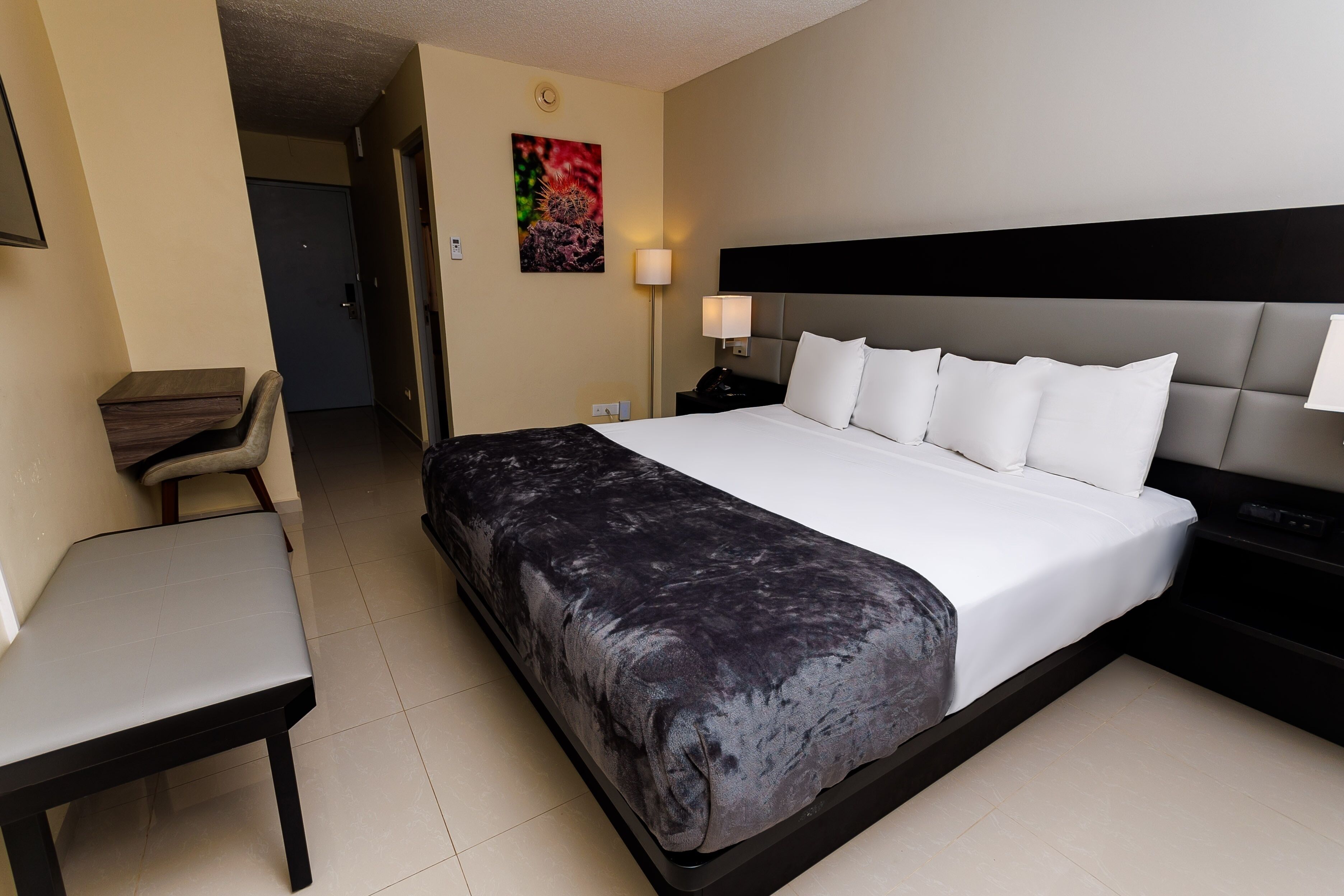 A hotel room with a bed, a desk, a chair, and a nightstand.