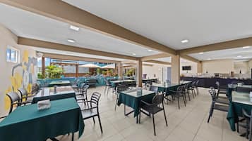 Un amplio comedor interior con varias mesas y sillas, vistas al exterior y una mesa de buffet.