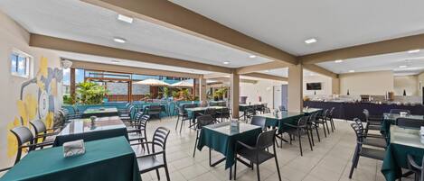Un amplio comedor interior con varias mesas y sillas, vistas al exterior y una mesa de buffet.