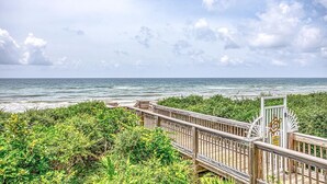 Un paseo marítimo de madera que conduce a una playa con vistas al océano y al cielo.