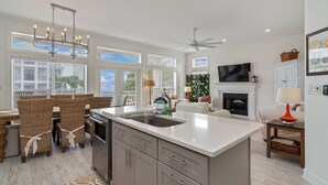 Una cocina moderna con una isla grande, comedor con sillas de mimbre, chimenea y televisor.