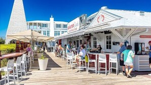 Un restaurante costero con terraza, un edificio blanco destacado con techo a dos aguas y un cielo azul despejado.
