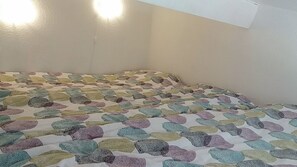A bed with a colorful, patterned bedspread in a room with white walls and two wall-mounted lights.