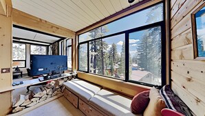 L’intérieur d’une cabane avec une grande fenêtre, des murs en bois, un téléviseur et une cheminée en pierre.