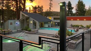 Ein Poolbereich mit einem kleinen Gebäude, einer umzäunten Terrasse und Blick auf Bäume und einen Sonnenuntergang.
