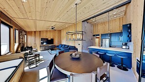 Eine moderne Küche mit Holzausbau, einer zentralen Kochinsel mit Sitzgelegenheiten, einem großen Flachbildfernseher und einem Deckenventilator.