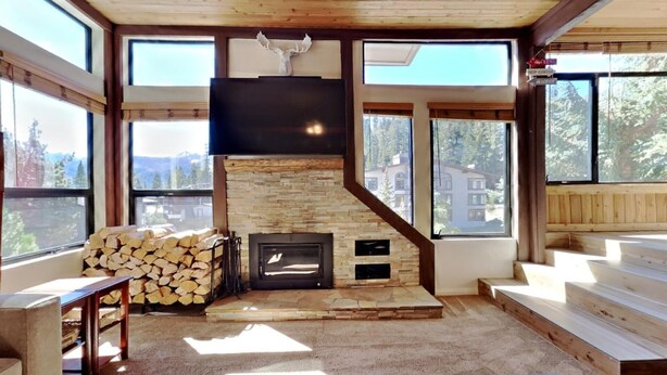 A spacious living room with a stone fireplace, large windows offering a view of the surrounding area, and a mounted television above the fireplace. - Spacious 2 Bedroom Condo Great For Friends and Families! Hiking, Swimming, Stargazing! by RedAwning (Mammoth Lakes)