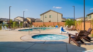 Un área de piscina con sillones reclinables y un jacuzzi, rodeada de casas y un cielo despejado.