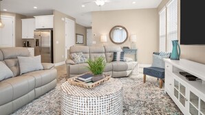 Un salón moderno con un sofá color beige, una mesa de centro redonda y un televisor sobre un mueble blanco.