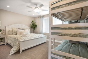 Ein Schlafzimmer mit Etagenbett, Deckenventilator, Zimmerpflanze und einem Fenster mit Jalousien.