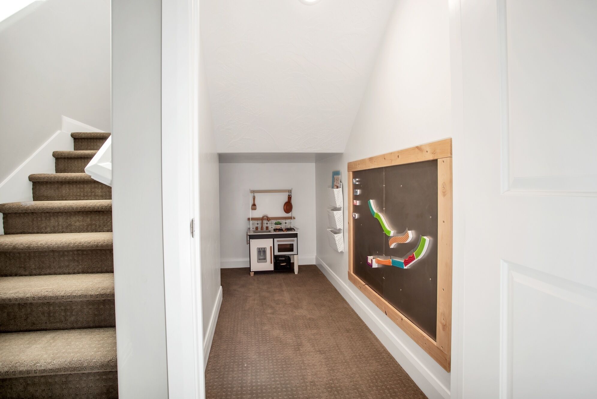 Un pasillo con una escalera alfombrada, una zona de cocina con microondas y una pared con pizarra.