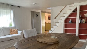 Un salon avec une table ronde en bois, un canapé blanc et un escalier doté d’étagères rouges.