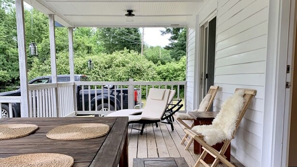 Une terrasse en bois avec une table et des chaises, une balustrade blanche et une vue sur la verdure.
