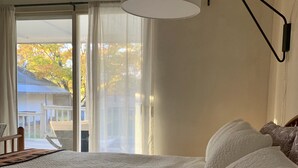 Une chambre avec un grand lit, un lampadaire au plafond et une vue sur une maison par la fenêtre.