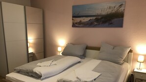 Un lit bien fait, avec des oreillers et des serviettes pliées, une lampe de chevet et un tableau accroché au mur.