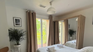 A bedroom with a bed, a chair, a desk, a potted plant, a mirror, and a view of the outdoors.