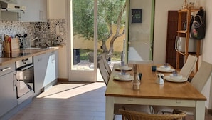 A modern kitchen with a dining area, featuring a large table set for four, a built-in oven, and a sliding glass door leading to an outdoor area.