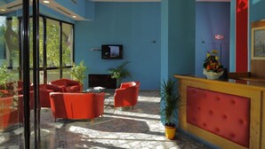 Um hall com cadeiras vermelhas, uma televisão na parede e uma receção com uma planta.