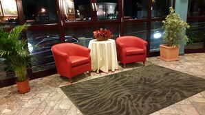 Um hall de entrada com duas poltronas vermelhas, uma mesa redonda com toalha branca e um tapete estampado.