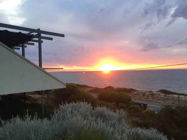 Un coucher de soleil sur l’océan, avec vue sur la mer et un bâtiment agrémenté d’une pergola.