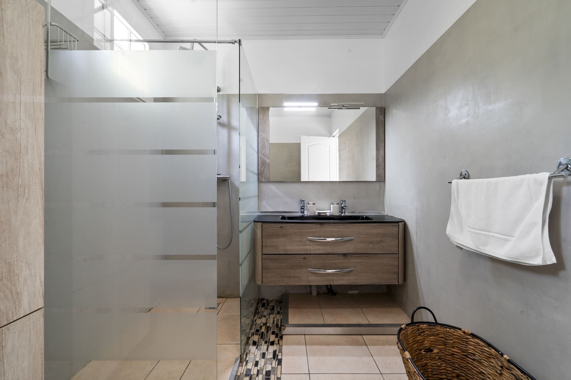 A bathroom with a shower, a sink, a mirror, and a towel hanging on the wall.