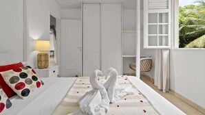 A bedroom with a bed, a nightstand, a lamp, a window with a view of greenery, and a door. - Nature Paradise - Four Bedroom Villa, Sleeps 8 (Rivière-Pilote)