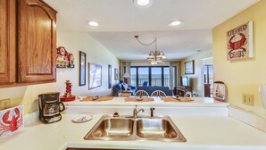 A kitchen with a double sink, wooden cabinets, and a dining area with a view of the ocean.
