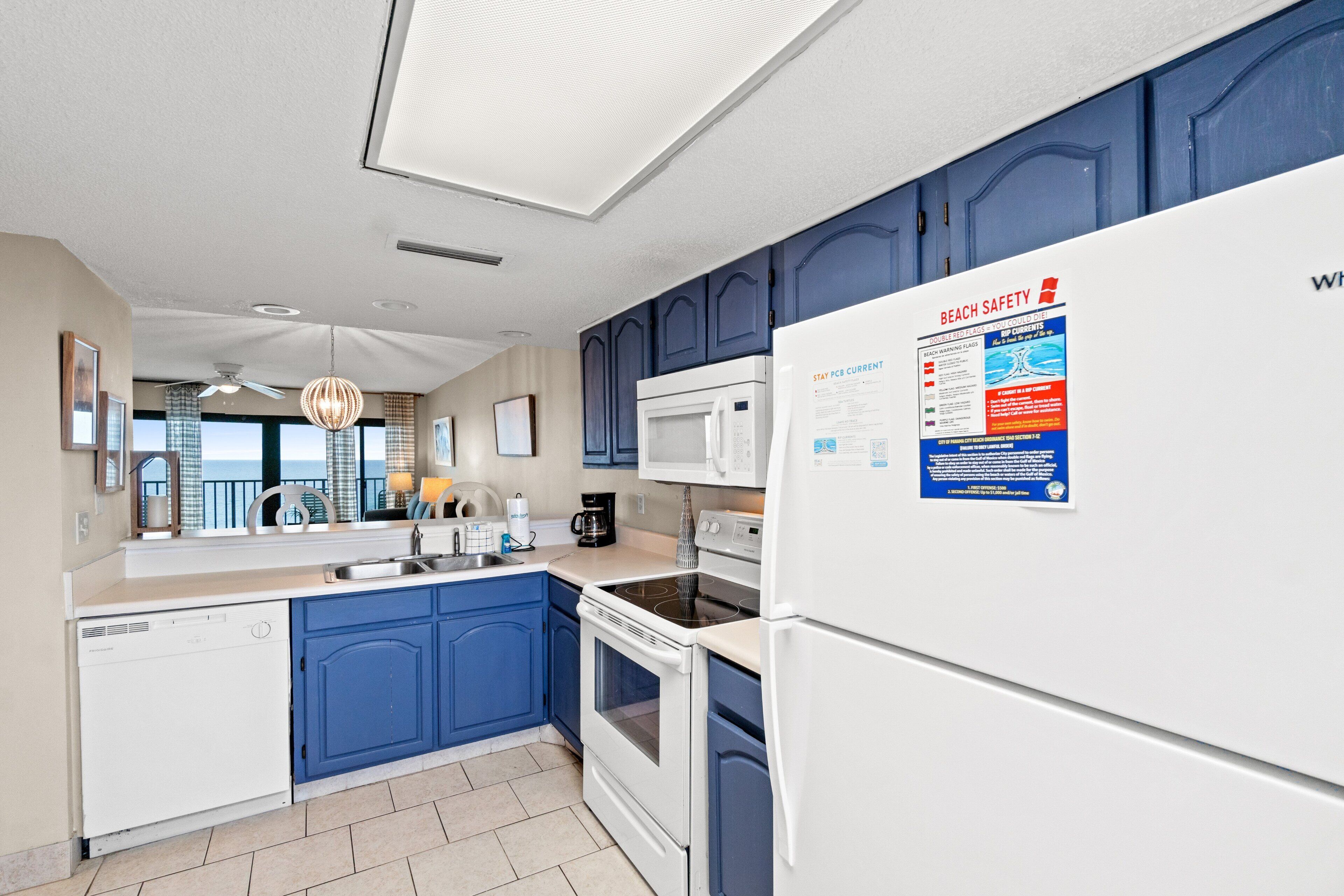 A modern kitchen with blue cabinets, white appliances, and a view of the ocean.