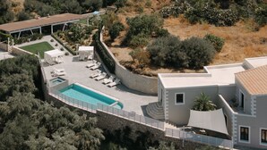Eine Vogelperspektive zeigt eine moderne Villa mit Swimmingpool, Liegestühlen und einer überdachten Terrasse.