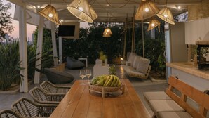 Ein Essbereich im Freien mit Korbmöbeln, einem Holztisch und hängenden Lampen aus Korbgeflecht.
