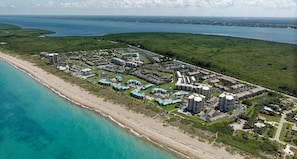 An aerial view of a coastal resort with multiple buildings, a beach, and surrounding greenery.