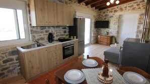 A stone-walled kitchen with wooden cabinets, a stainless steel sink, a built-in oven, and a dining table set with plates and a bottle.