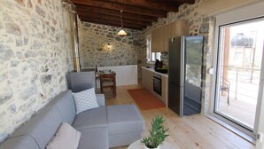 A cozy living area with a stone wall, a grey sofa, a small dining table, and a kitchen with a refrigerator.