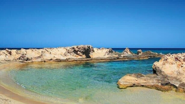 A beach with clear water, rocky formations, and a sandy shore.