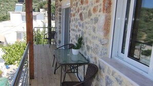 A balcony with a wooden floor, stone wall, and a glass table with chairs.