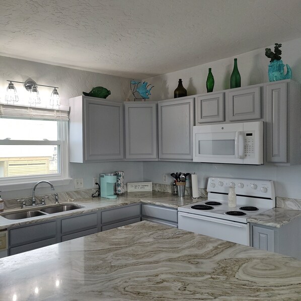 A kitchen with white cabinets, a microwave, a stove, and a sink.