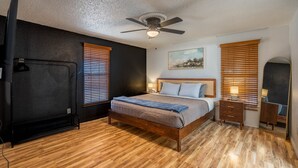 A bedroom with a wooden floor, a bed with a headboard, a ceiling fan, and two bedside tables with lamps.