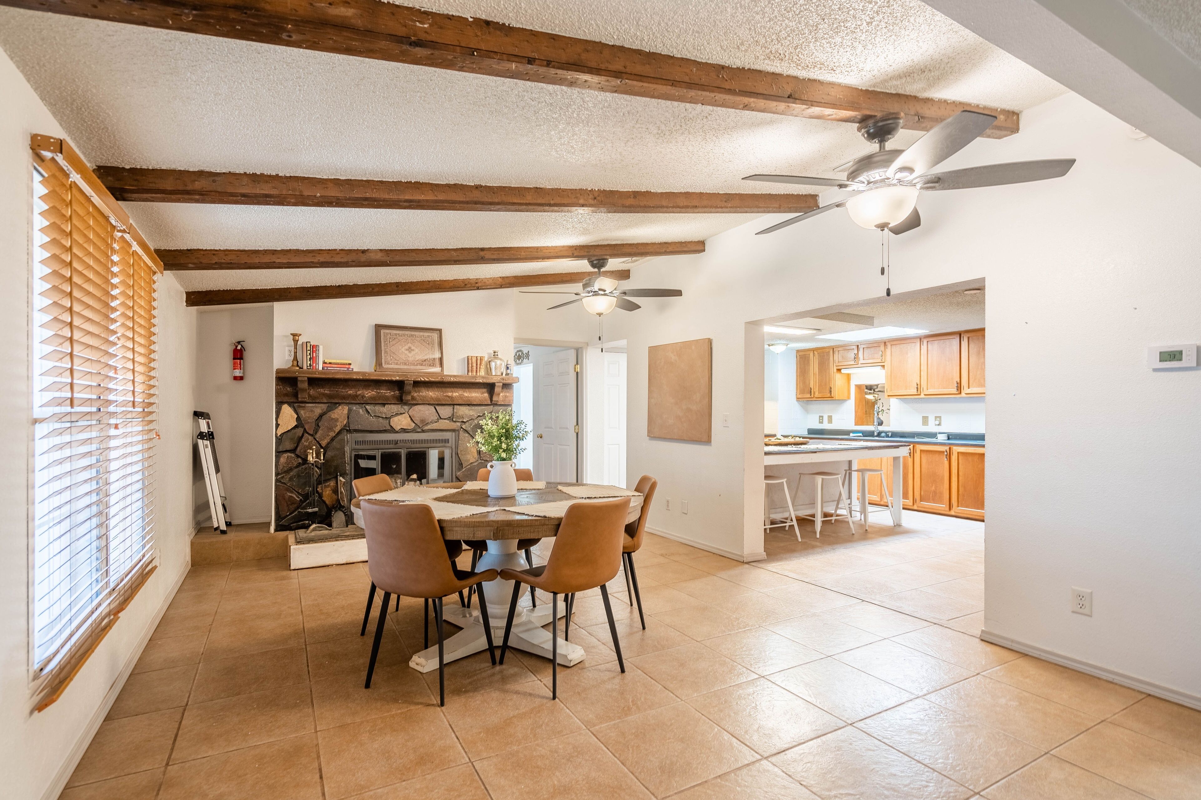 A dining area with a stone fireplace, wooden beams, and a ceiling fan.