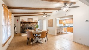 A dining area with a stone fireplace, wooden beams, and a ceiling fan.