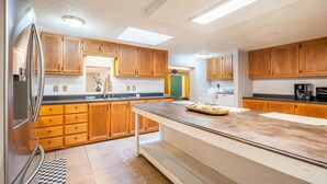 A modern kitchen with wooden cabinets, a stainless steel refrigerator, a large island, and a view of the laundry room.