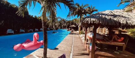 A poolside area with lounge chairs, a wooden deck, and a thatched-roof hut.