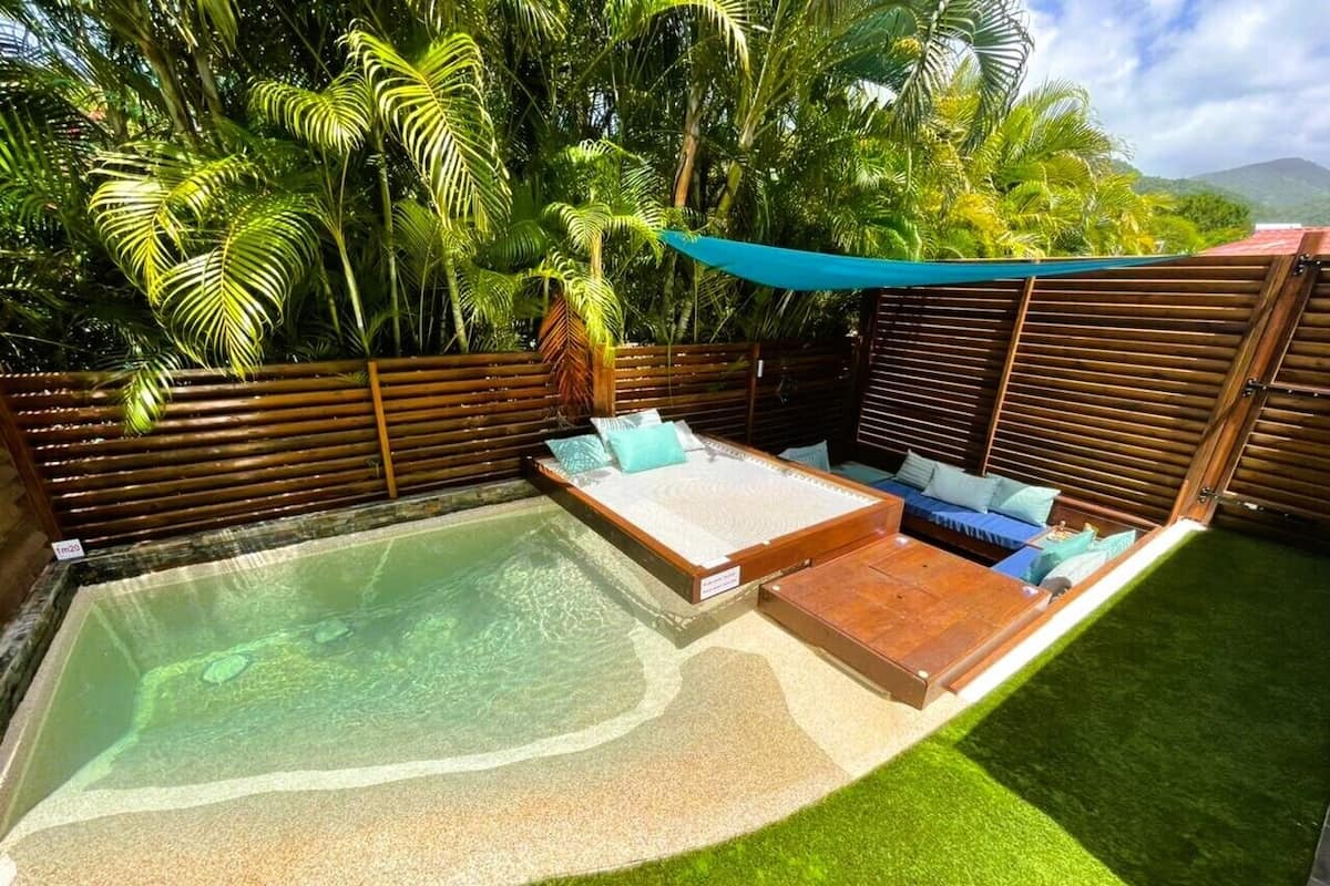 A backyard with a hot tub, a wooden deck, and a seating area with cushions.