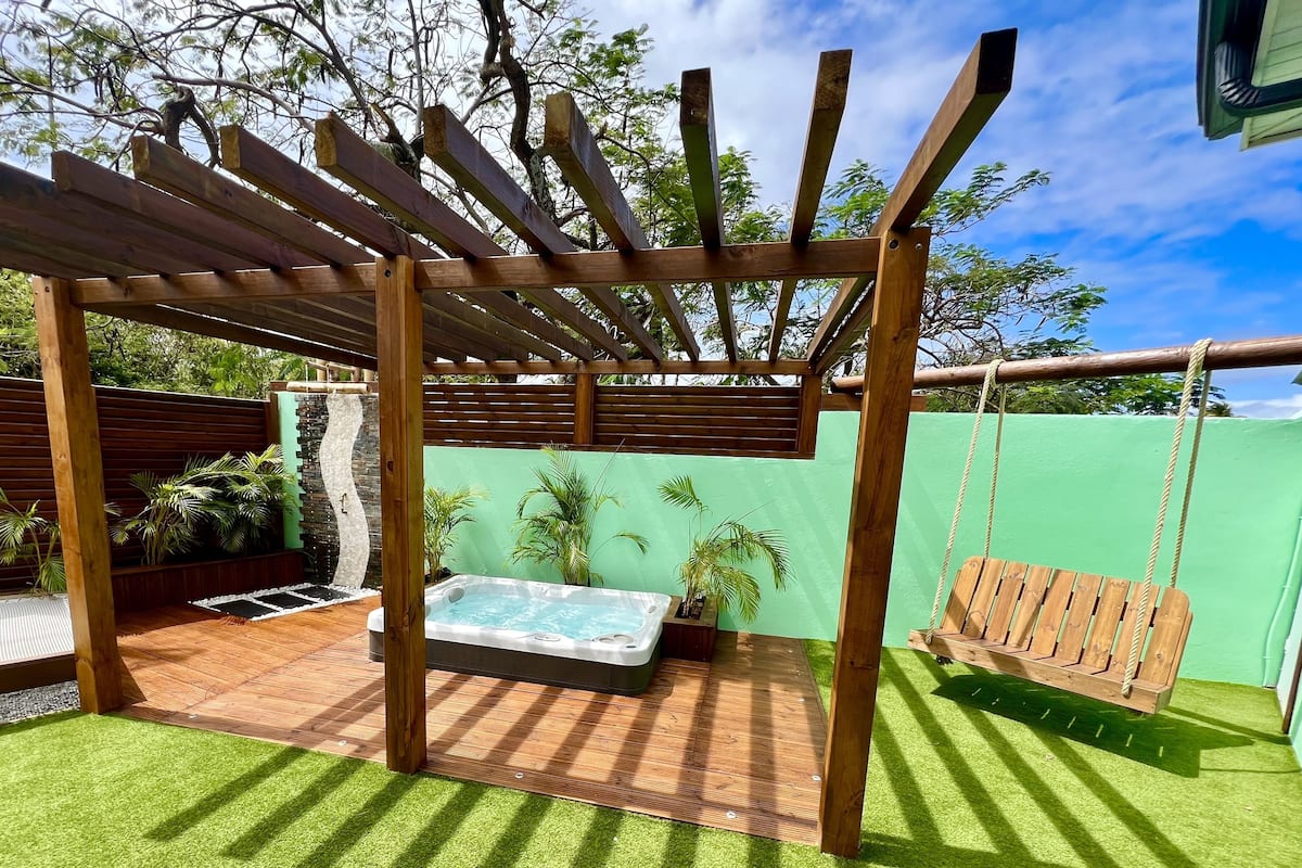 A wooden pergola with a swing, a hot tub, and a green wall.