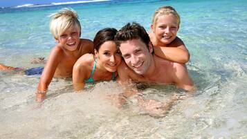 A family of four in clear, shallow water at a beach.